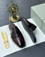 A pair of luxurious black leather half shoes displayed on a white surface, accompanied by a small Italian flag keychain and a stylish gold ship's wheel, evoking a sense of high-end elegance.
