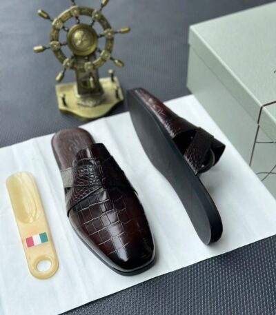 A pair of luxurious black leather half shoes displayed on a white surface, accompanied by a small Italian flag keychain and a stylish gold ship's wheel, evoking a sense of high-end elegance.