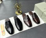 A pair of luxurious black leather half shoes displayed on a white surface, accompanied by a small Italian flag keychain and a stylish gold ship's wheel, evoking a sense of high-end elegance.