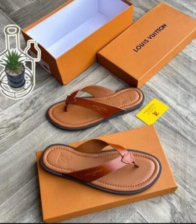 A pair of luxurious leather sandals displayed on a wooden floor, accompanied by an open orange shoe box bearing the Louis Vuitton logo, showcasing the epitome of high-end footwear.