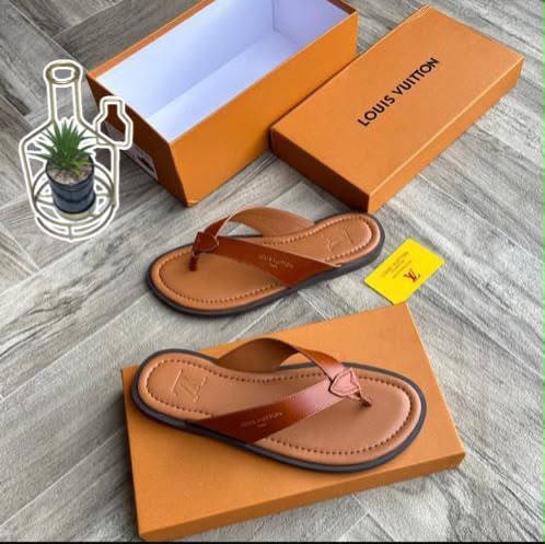 A pair of luxurious leather sandals displayed on a wooden floor, accompanied by an open orange shoe box bearing the Louis Vuitton logo, showcasing the epitome of high-end footwear.