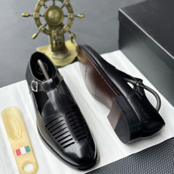 A pair of black leather monk strap shoes on a white cloth, accompanied by a shoe tree and a decorative ship's wheel in the background.