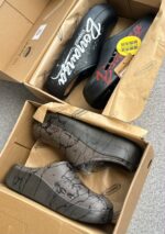 A pair of stylish black and grey shoes with distinctive designs, placed on a grey surface next to a shoe box.