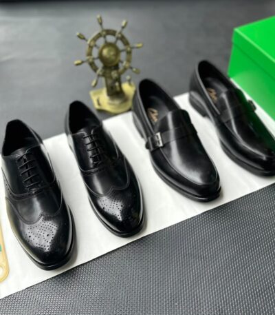 A pair of black leather oxfords with brogue detailing, accompanied by a shoe tree and presented on a crisp white background.