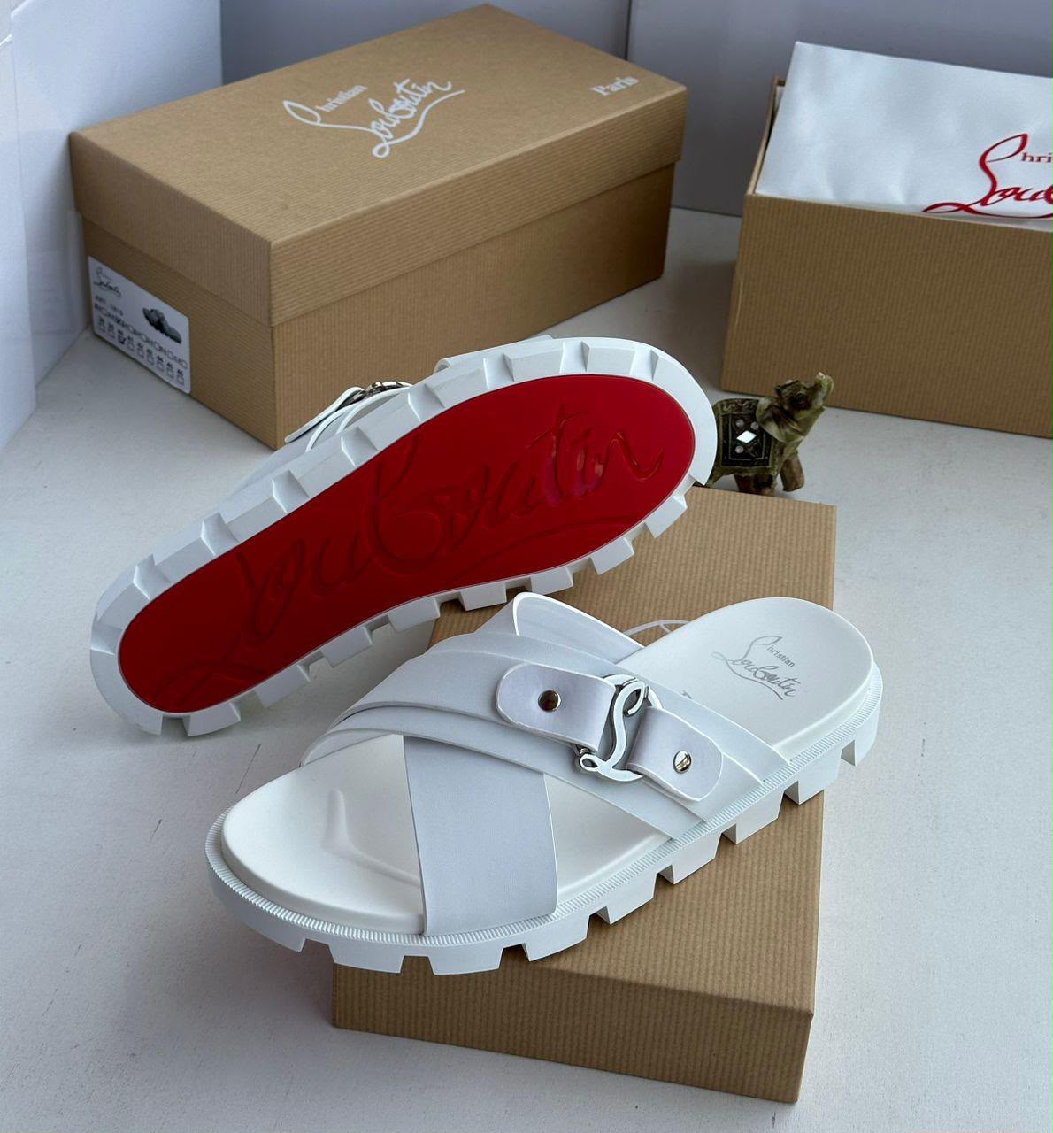 root A pair of pristine white slides with a striking red sole, nestled on a brown shoe box, exuding high-end sophistication.