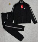 A stylish black tracksuit with grey accents and Nike logo, laid out on a grey surface.