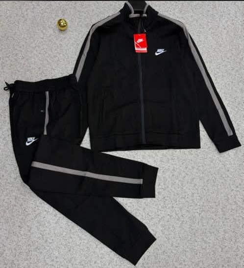 A stylish black tracksuit with grey accents and Nike logo, laid out on a grey surface.