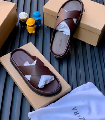 A pair of luxurious brown leather slides on top of shoe boxes, exuding high-end quality and comfort.