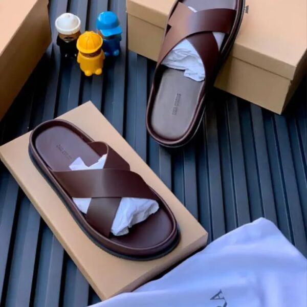 A pair of luxurious brown leather slides on top of shoe boxes, exuding high-end quality and comfort.