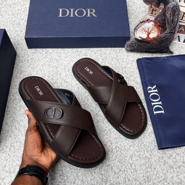 A pair of luxurious dark brown Dior slide sandals with a sleek design and iconic CD logo, presented with a blue box and dust bag.