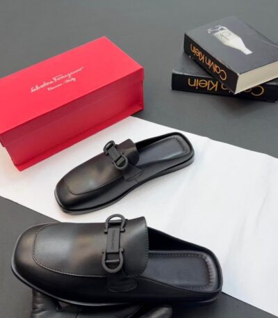 A pair of luxurious black leather loafers displayed with a red shoe box and two fashion books, embodying high-end style and comfort.