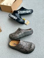 A pair of stylish black and grey shoes with distinctive designs, placed on a grey surface next to a shoe box.