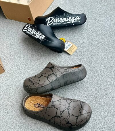 A pair of stylish black and grey shoes with distinctive designs, placed on a grey surface next to a shoe box.
