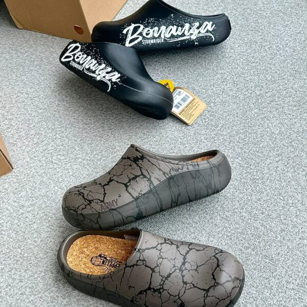 A pair of stylish black and grey shoes with distinctive designs, placed on a grey surface next to a shoe box.