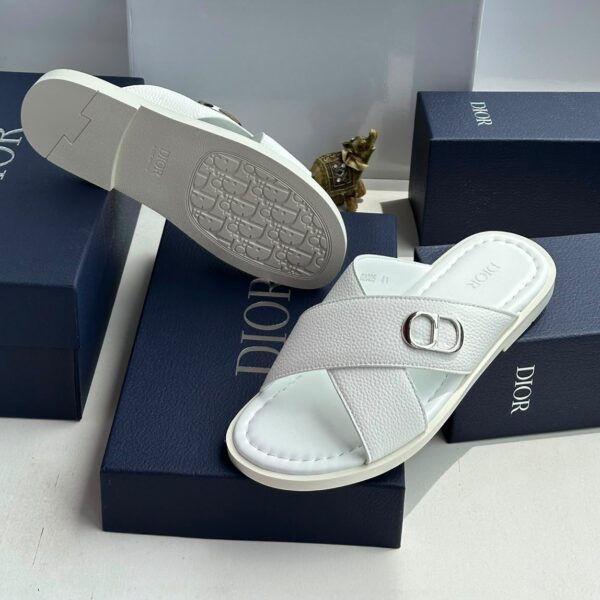 A pair of white leather slides with a silver 'CD' buckle, displayed on navy blue boxes with the 'DIOR' logo.