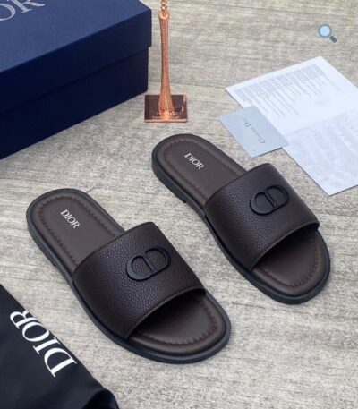 A pair of luxurious Dior slides with a sleek design and iconic logo, presented with a box and accessories.