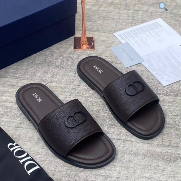 A pair of luxurious Dior slides with a sleek design and iconic logo, presented with a box and accessories.