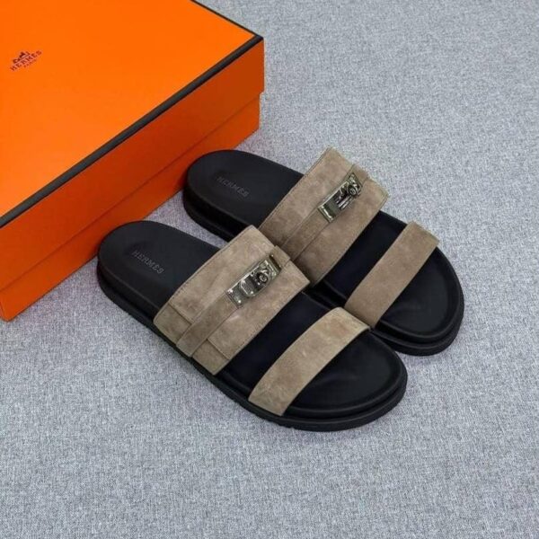A pair of luxurious black slides with tan suede straps and silver buckles, accompanied by an orange shoe box on a light grey background.