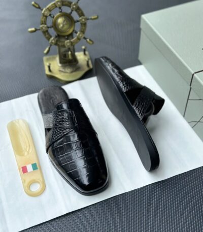 A pair of luxurious black leather half shoes displayed on a white surface, accompanied by a small Italian flag keychain and a stylish gold ship's wheel, evoking a sense of high-end elegance.