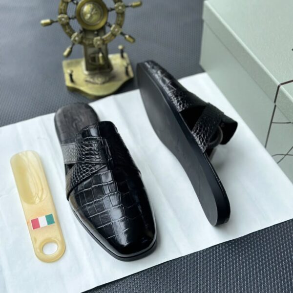 A pair of luxurious black leather half shoes displayed on a white surface, accompanied by a small Italian flag keychain and a stylish gold ship's wheel, evoking a sense of high-end elegance.