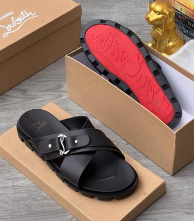 A pair of luxurious black slide sandals with a red sole, nestled in a brown shoe box alongside a golden dog statue and books.
