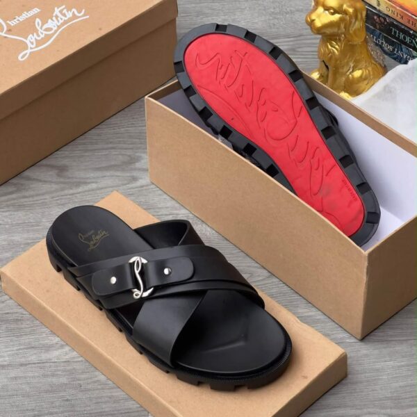A pair of luxurious black slide sandals with a red sole, nestled in a brown shoe box alongside a golden dog statue and books.