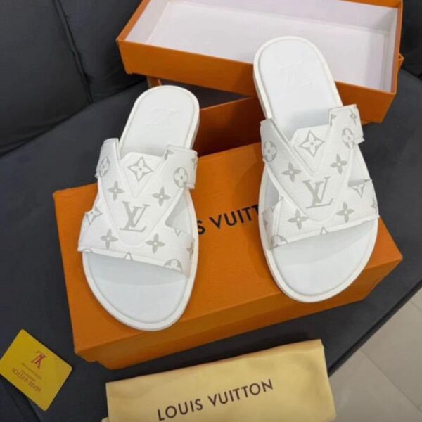 A pair of white Louis Vuitton slides with monogram pattern on a black couch with an open orange box and dust bag.