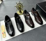 A pair of black leather monk strap shoes on a white cloth, accompanied by a shoe tree and a decorative ship's wheel in the background.