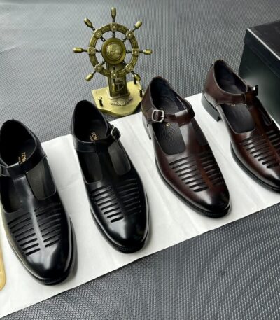 A pair of black leather monk strap shoes on a white cloth, accompanied by a shoe tree and a decorative ship's wheel in the background.
