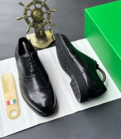 A pair of black leather oxfords with brogue detailing, accompanied by a shoe tree and presented on a crisp white background.