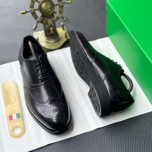 A pair of black leather oxfords with brogue detailing, accompanied by a shoe tree and presented on a crisp white background.