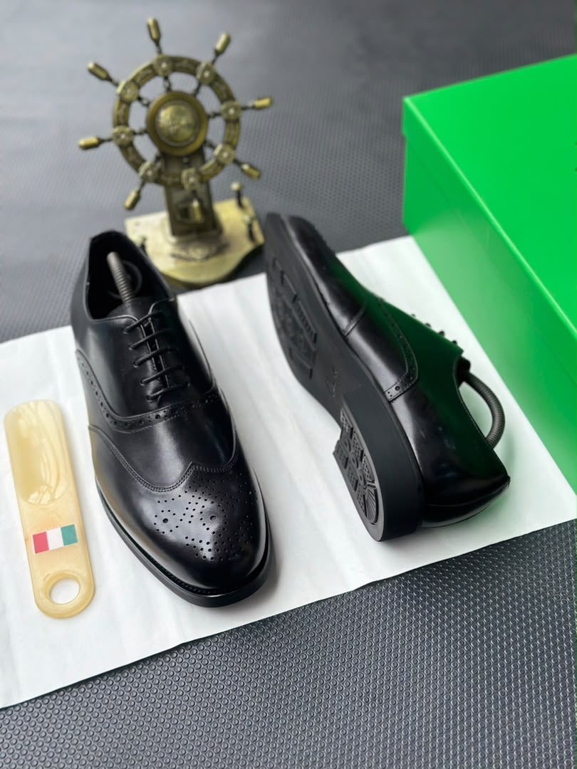 root A pair of black leather oxfords with brogue detailing, accompanied by a shoe tree and presented on a crisp white background.