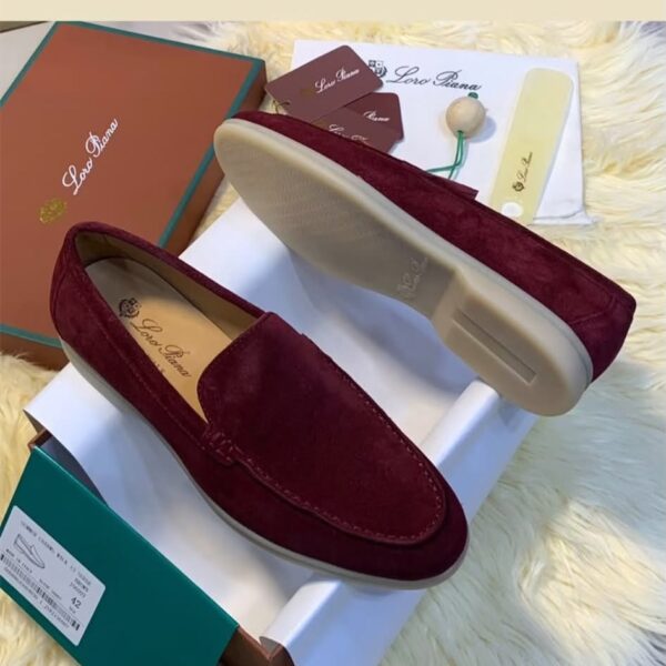 A pair of luxurious, maroon suede loafers showcased on a pristine white box, accompanied by a matching box, dust bag, and shoe care accessories, all set against a plush, cream-colored fur backdrop.