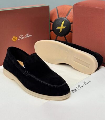 A pair of luxurious black velvet loafers with cream-colored soles, displayed on a pristine white surface alongside their elegant packaging.