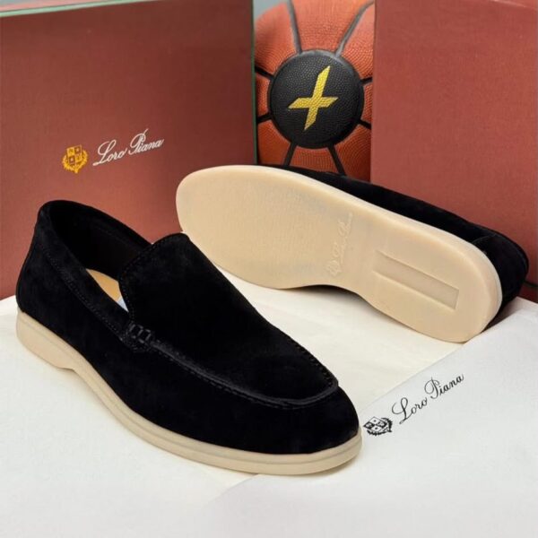 A pair of luxurious black velvet loafers with cream-colored soles, displayed on a pristine white surface alongside their elegant packaging.